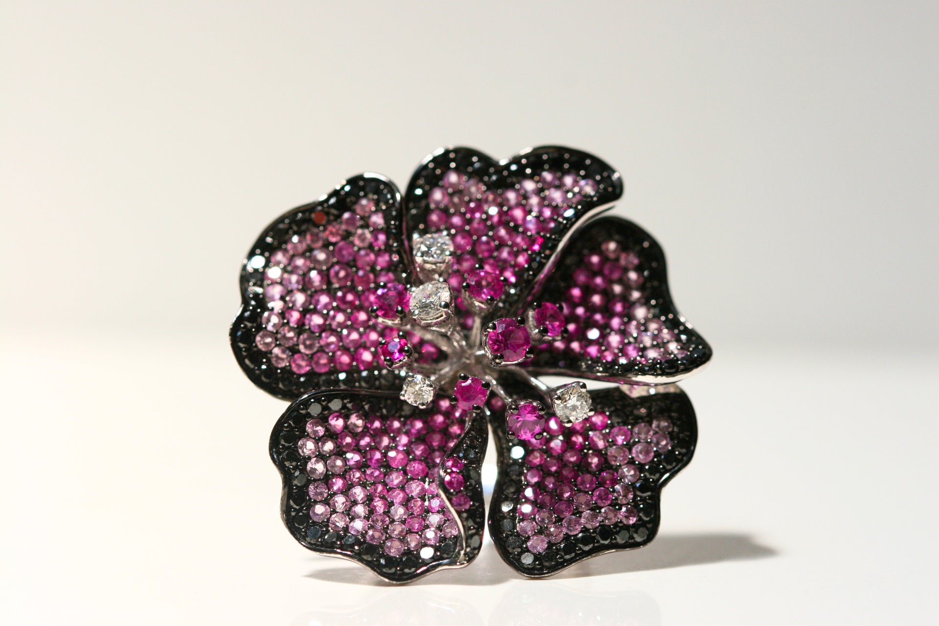 A statement flower ring. Varying shades of pink sapphires decorate the ring, along with black & white diamonds. There are stamen of the flowers that end in individual stones. Set in white gold, and some parts plated in black rhodium. Local SF jewelry, San francisco, Luxury, hand made, Bay area, gift for her, september birthstone