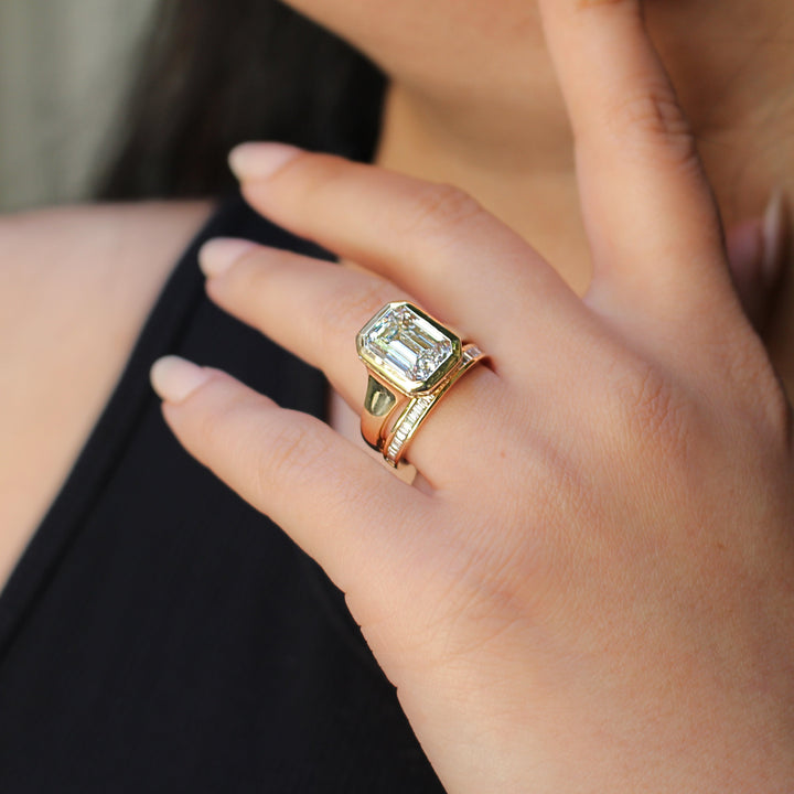 an emerald diamond bezel engagement ring stacked with a baguette diamond band on a hand model 