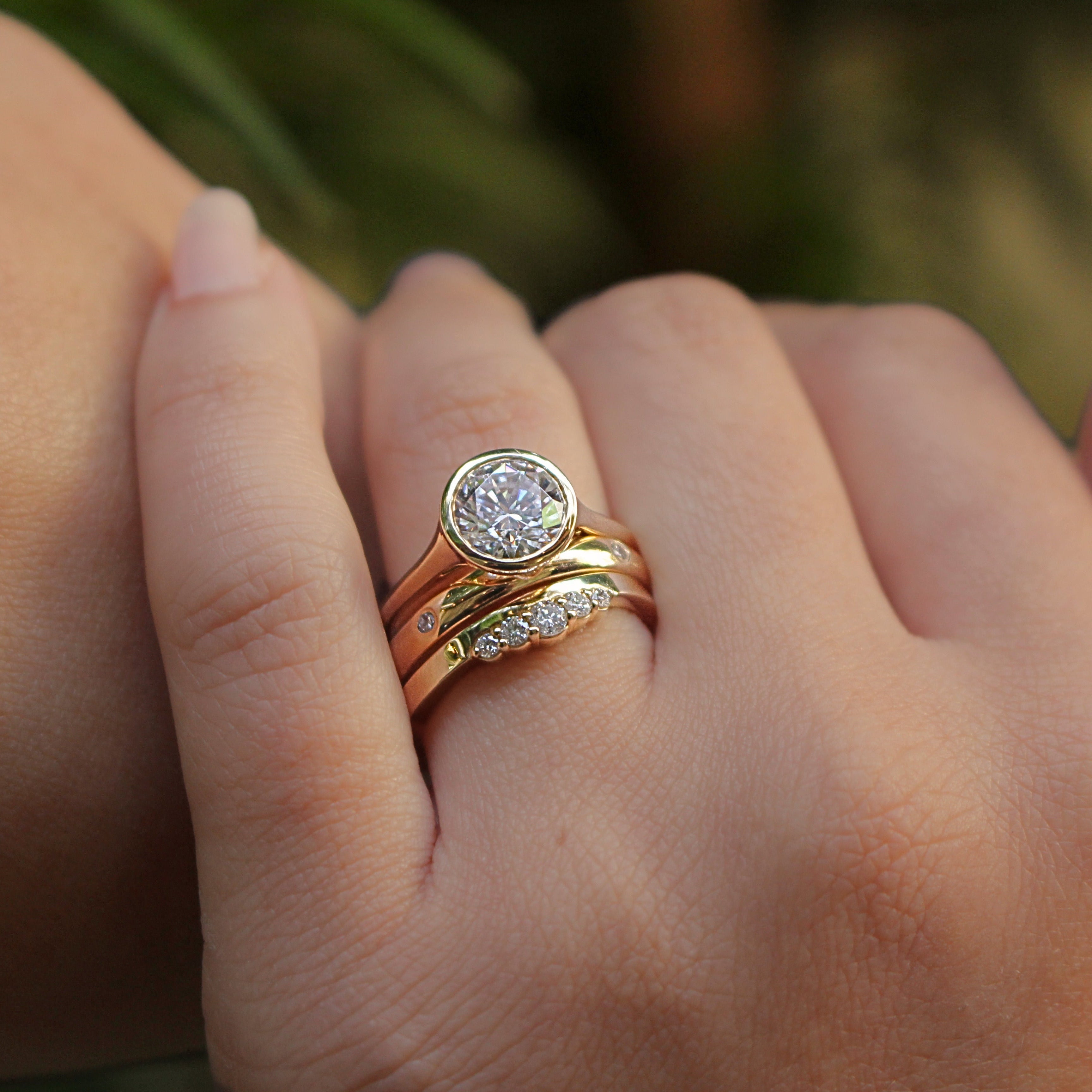 Yellow gold three ring stack worn on model with round bezel engagement ring, flush set eternity band, and flat diamond band