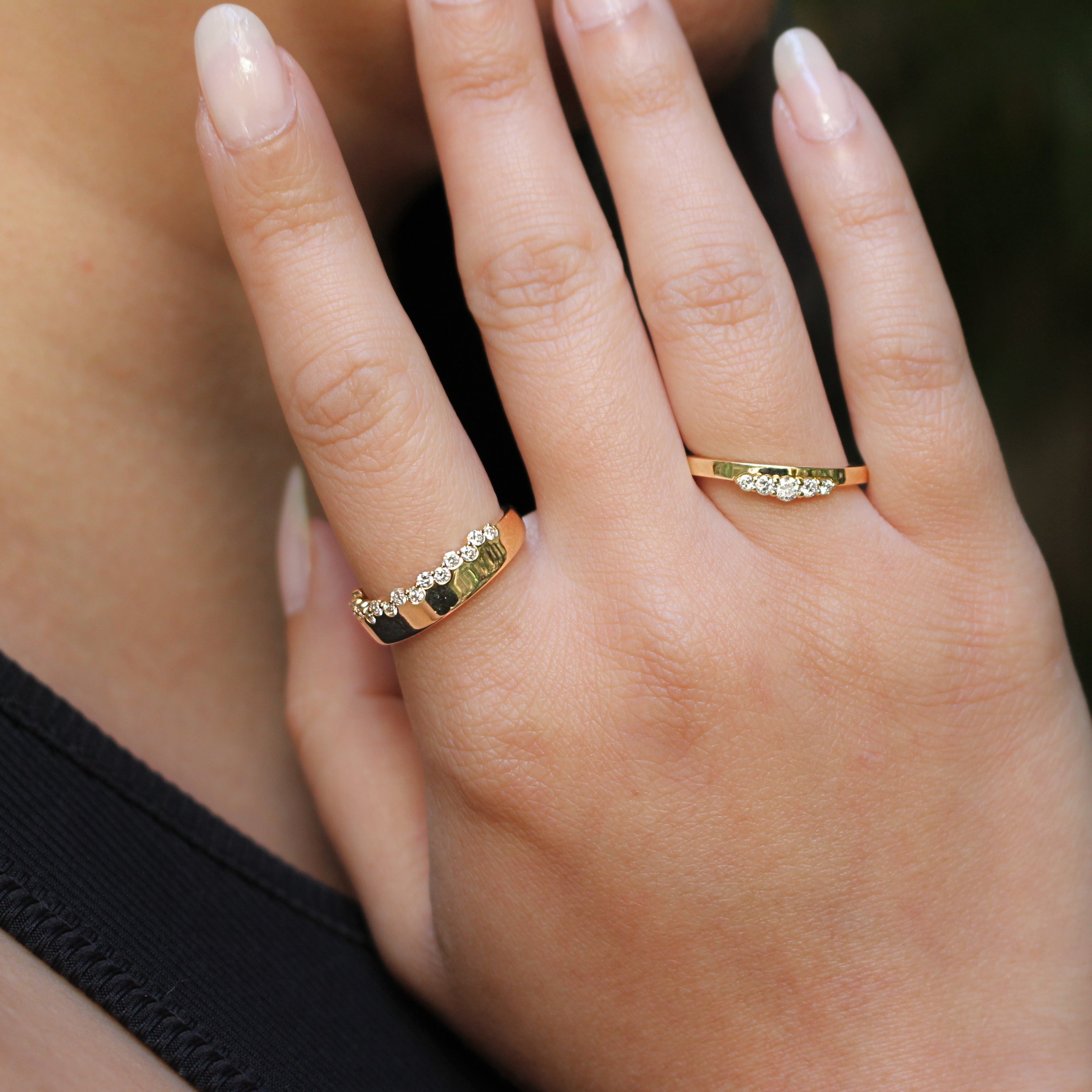 Close-up of a hand wearing two gold rings with  diamonds against a blurred background.