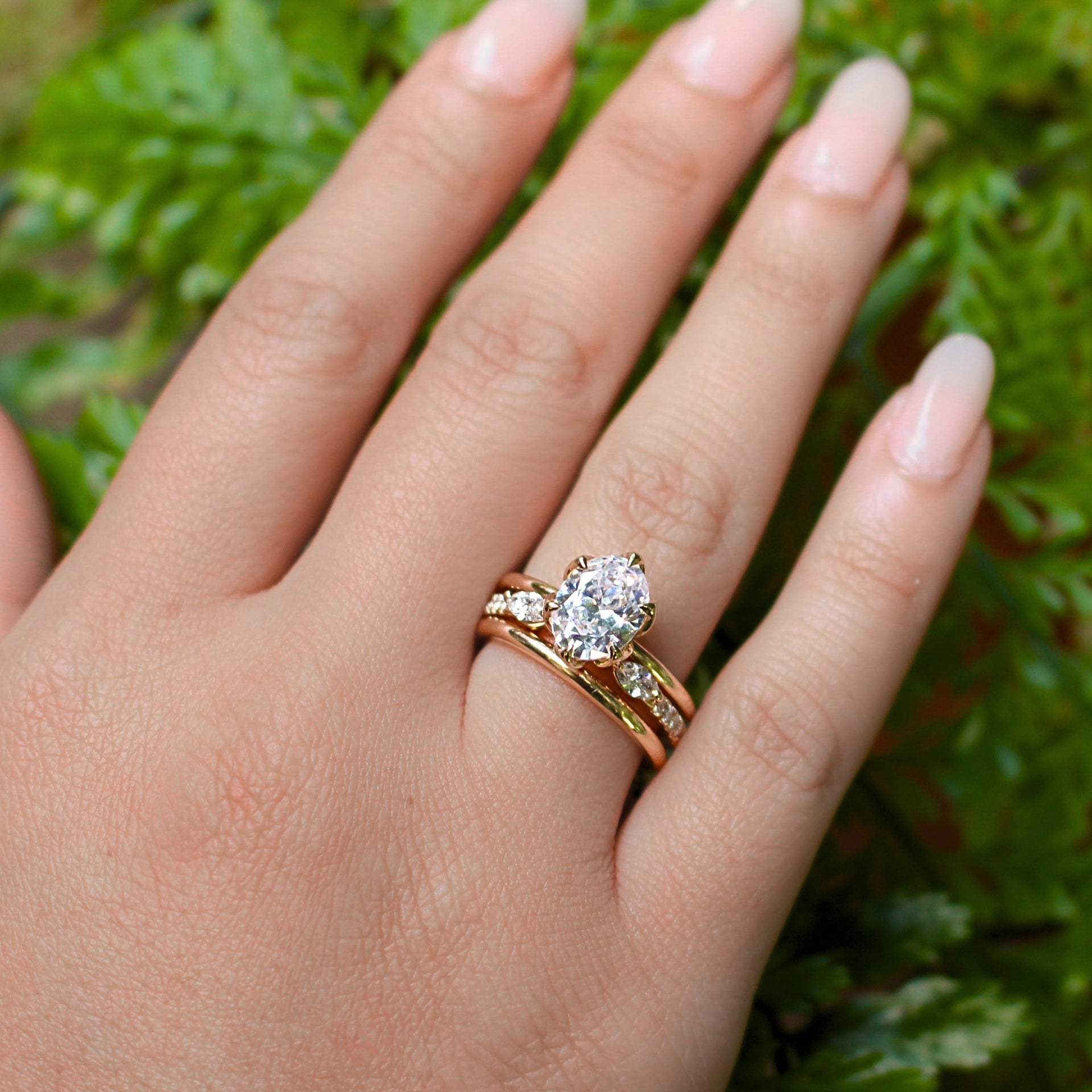 Hand wearing a gold three ring stack with a diamond on a green leafy background