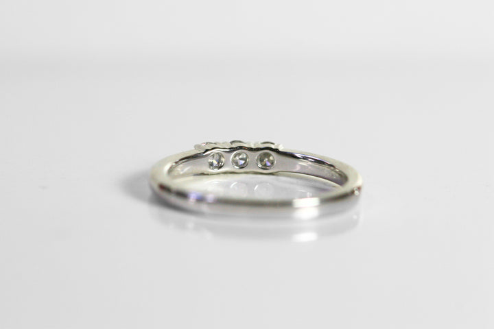 White gold ring with 3 round diamonds in the center. The band is the same thickness as the stones. This photo is a view of the back of the ring. 