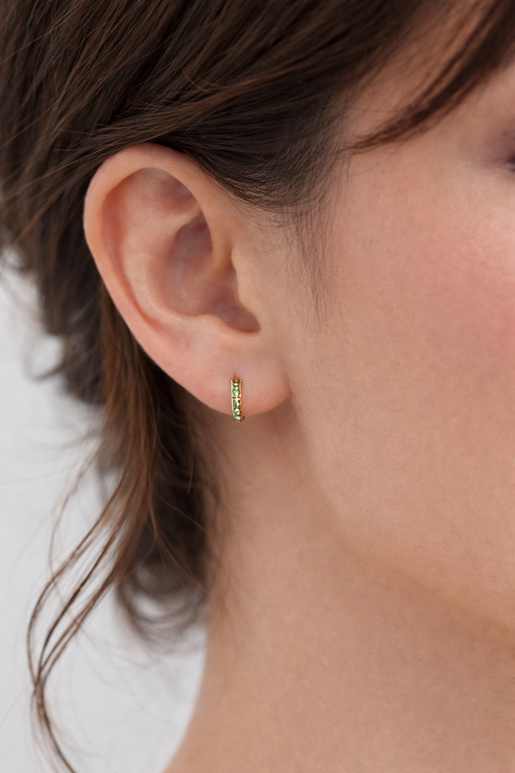 Close-up of an ear wearing a green hoop earring with a blurred background