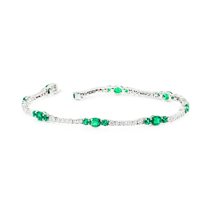 A white-gold tennis bracelet featuring round and Colombian green emerald gemstones, accented with small round diamonds, shown on a plain white background.