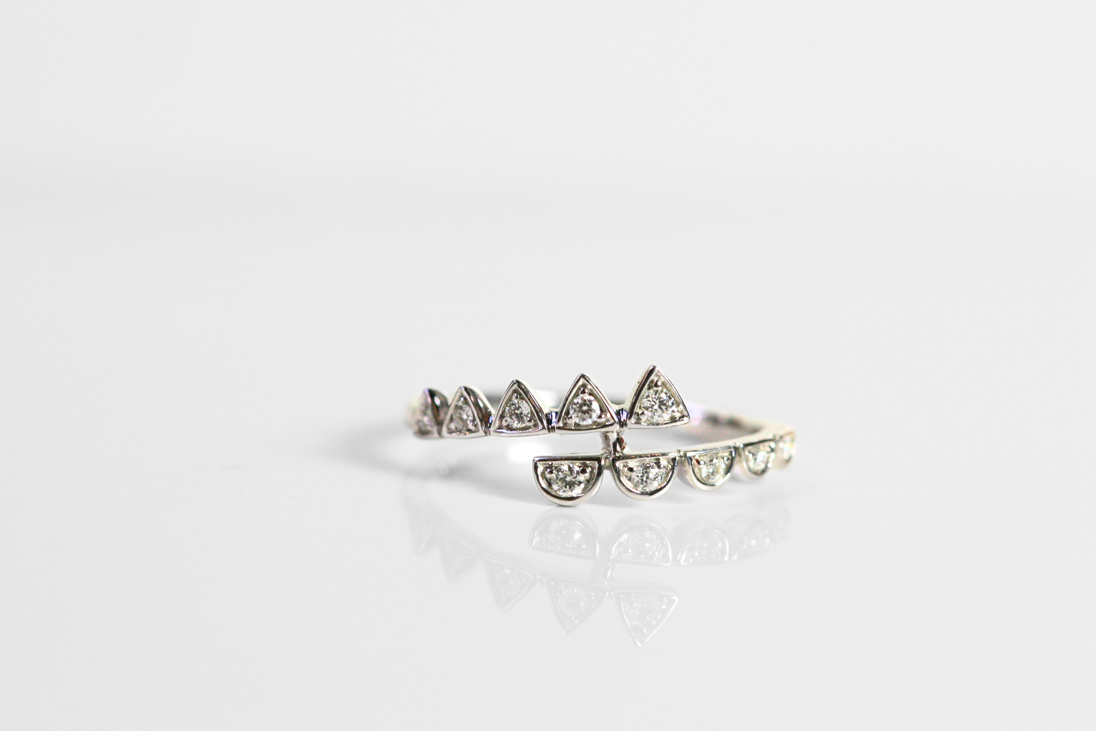 White gold ring with diamonds. Two arms wrap around the finger. Diamond triangles are on one arm, and half circles are on the other. Diamonds are round, brilliant cut stones.