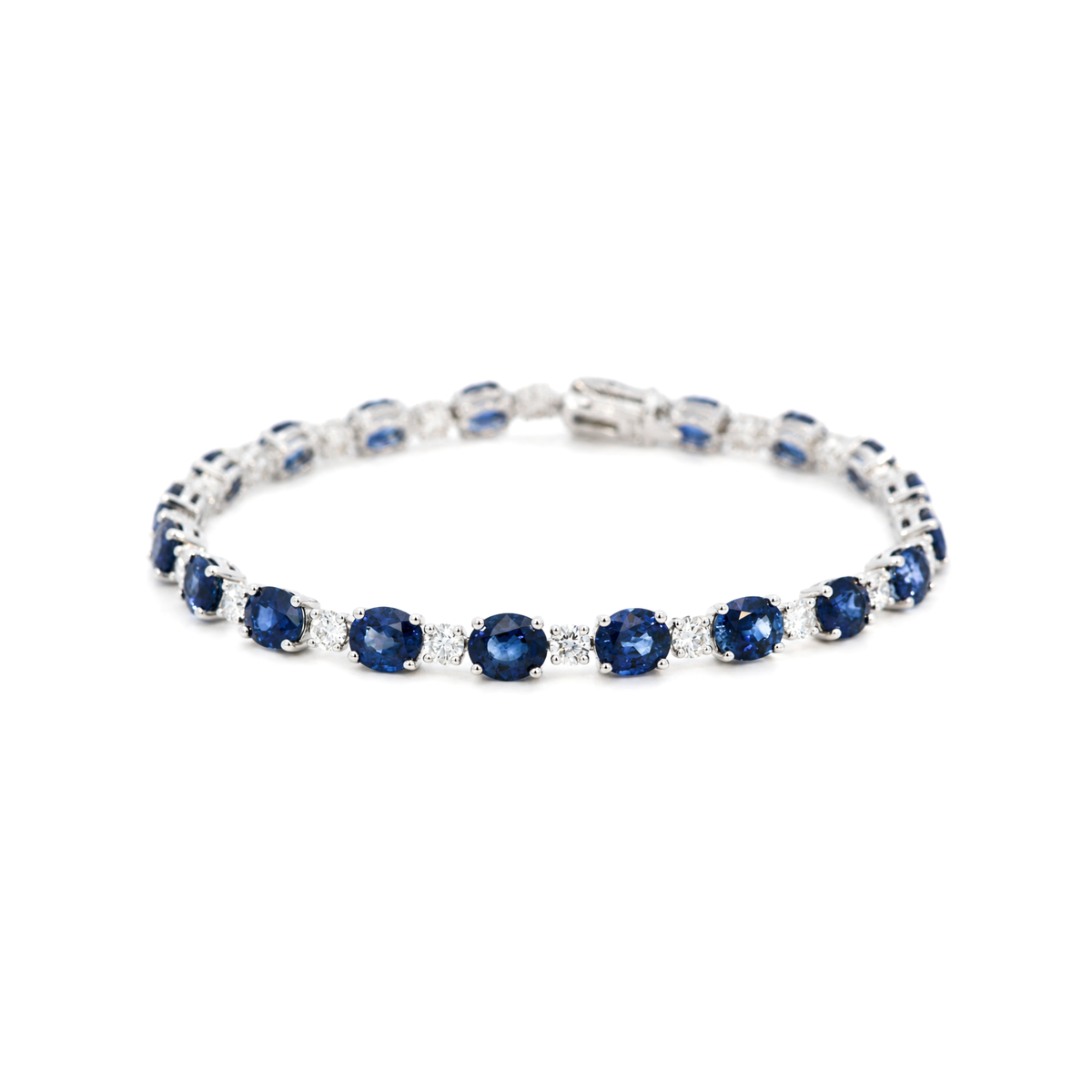 A tennis bracelet featuring alternating oval deep blue sapphires and round diamonds set in white gold, shown against a plain white background.