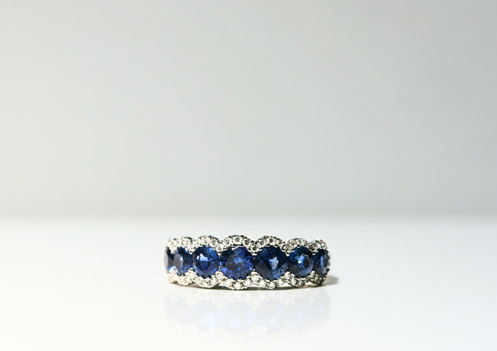 7 Round, deep blue sapphires. Each is framed by round, white diamonds that follow the curve of the stones. Set in white gold.