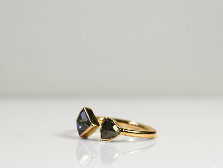 3/4 view of a black diamond ring set in yellow gold. The diamonds are bezel set and the band is fully rounded. They meet in the middle with a slight space between the two.