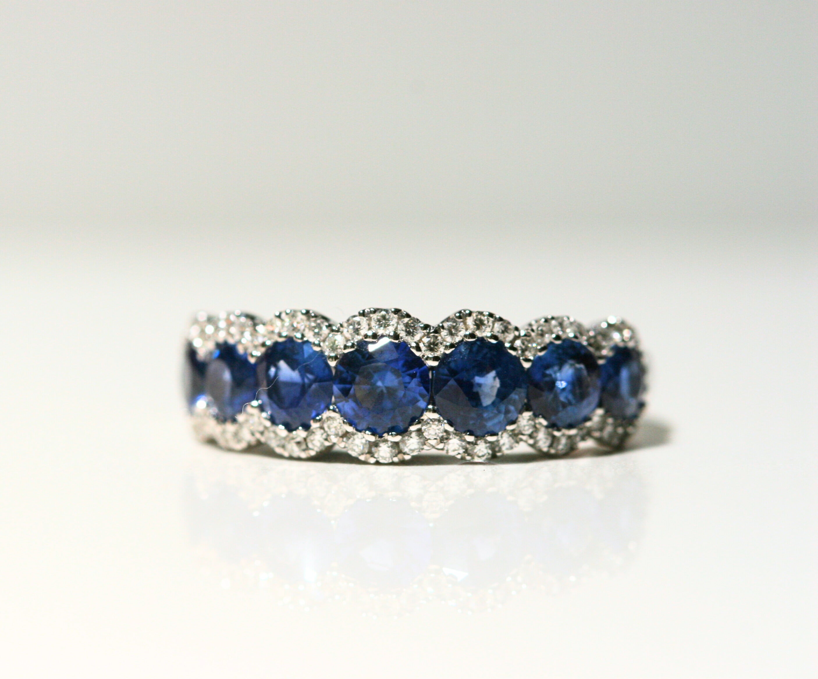 7 Round, deep blue sapphires. Each is framed by round, white diamonds that follow the curve of the stones. Set in white gold.