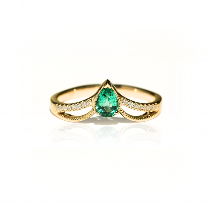 Gold ring with a pear-shaped emerald on a white background