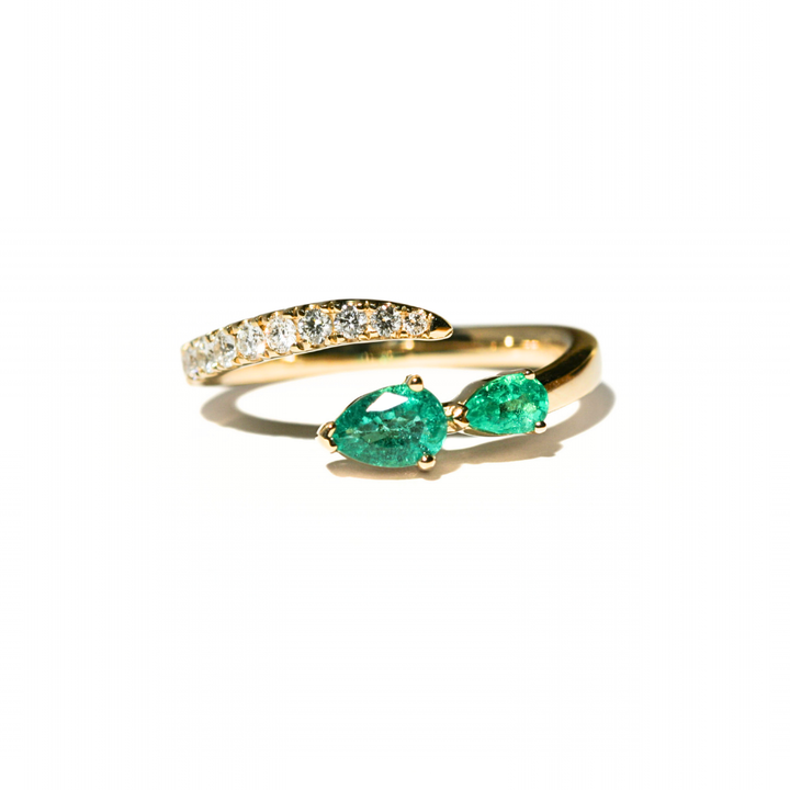 Gold ring with two pear-shaped emeralds on a white background