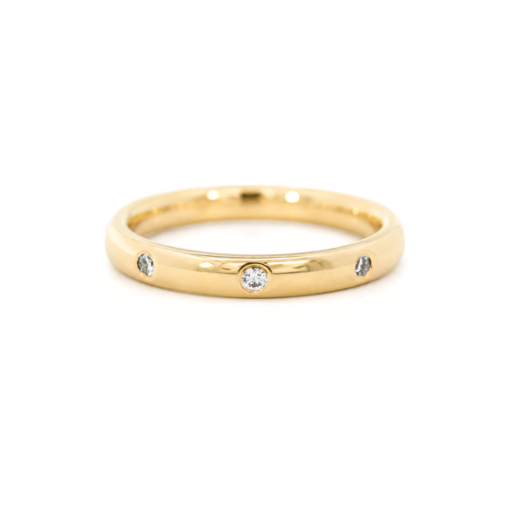 A yellow gold band ring featuring small round diamonds set into the band, photographed on a white background.