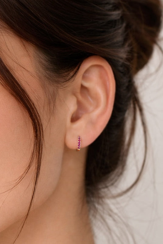 Close-up of a woman wearing a small ruby earring against a neutral background
