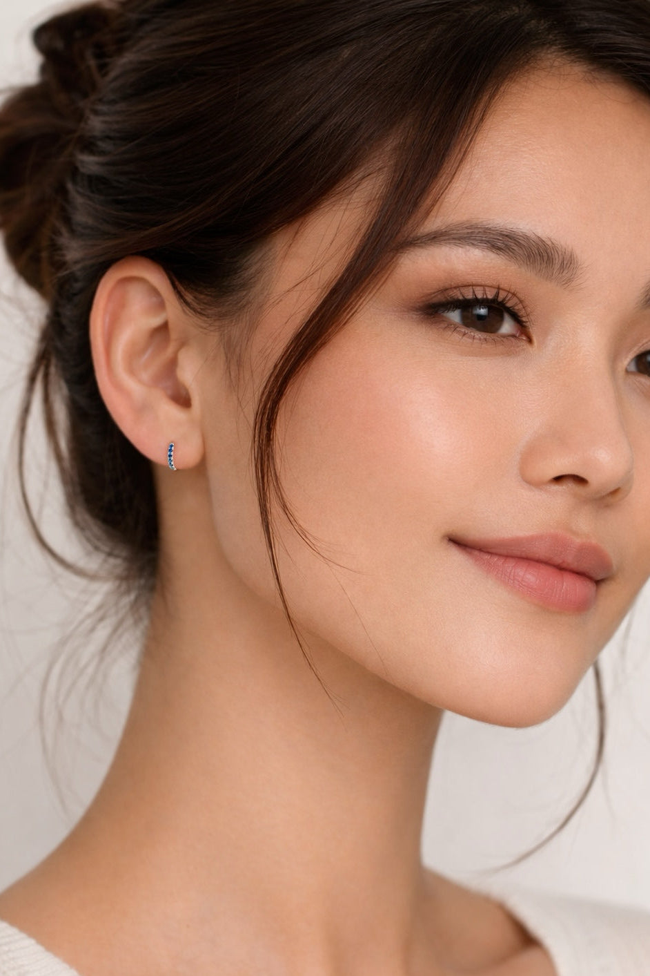 Close-up of a woman wearing a small sapphire huggie earring with a white background
